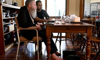 Rodney Gorham, who has a Synchron brain implant, works on a computer at his home in Melbourne with clinical field engineer Zafar Faraz